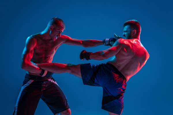 Tensioned. MMA. Two professional fighters punching or boxing isolated on blue studio background in neon. 