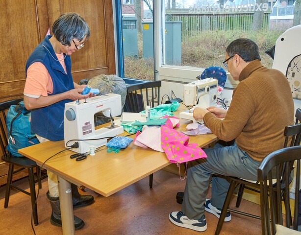 2 mensen zitten aan een tafel, beide met een naaimachine