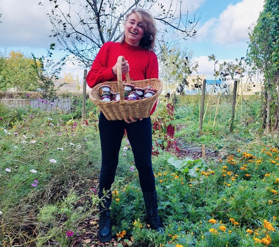 Een vrouw met een mand vol potten jam in haar hand in Wijktuin Noordhove