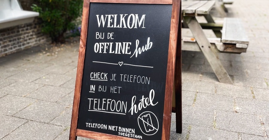 Reclamebord voor de Offline hub: "Welkom bij de Offline hub. Check je telefoon in bij het telefoonhotel. Telefoon niet binnen toegestaan"
